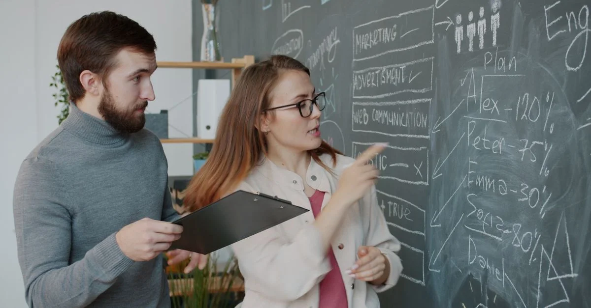 Deux collègues élaborent des stratégies sur les objectifs commerciaux autour d'un tableau noir.