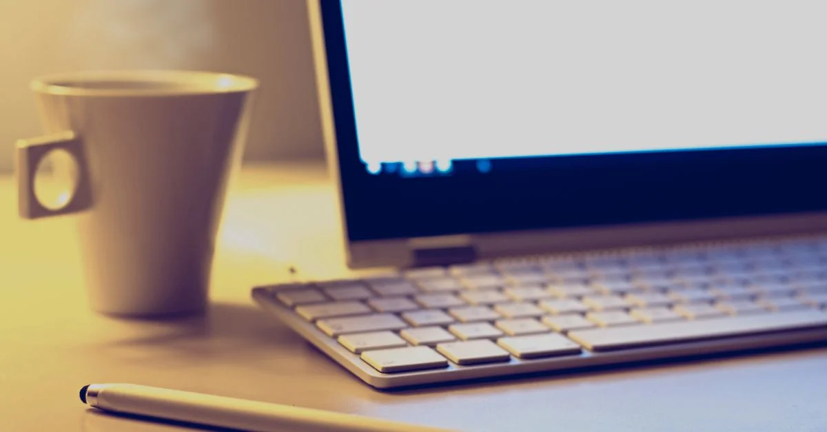 Configuration de bureau confortable avec un ordinateur portable, un clavier, un stylo et une tasse de café sur un bureau.