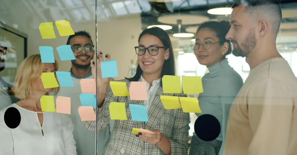 Des collègues de différents horizons collaborent dans un bureau en utilisant des post-it sur une paroi vitrée.