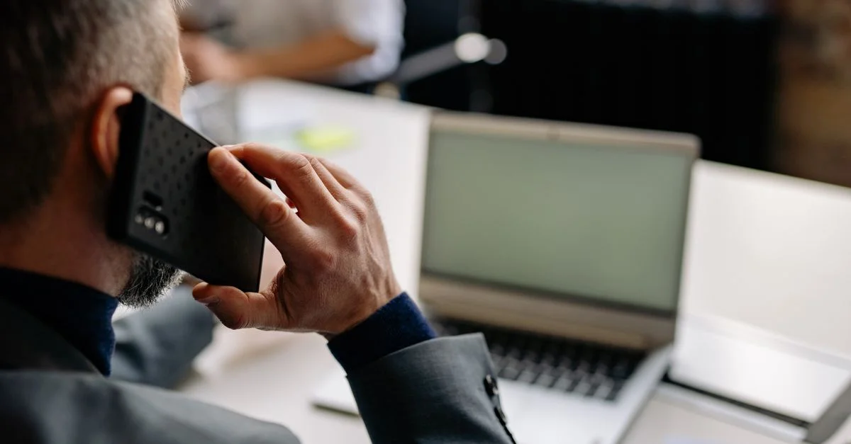 Homme professionnel utilisant un téléphone portable dans un bureau, multitâchant avec un ordinateur portable.