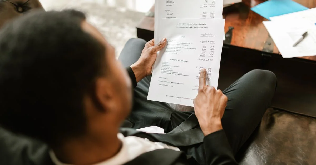 Professionnel des affaires examinant des documents financiers, se concentrant sur l'analyse et la paperasse dans un cadre de bureau.