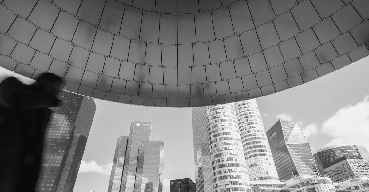 Une vue dynamique de la ligne d'horizon de La Défense à Paris, mettant en valeur des gratte-ciels modernes sous une arche métallique, suggérant une sophistication urbaine.