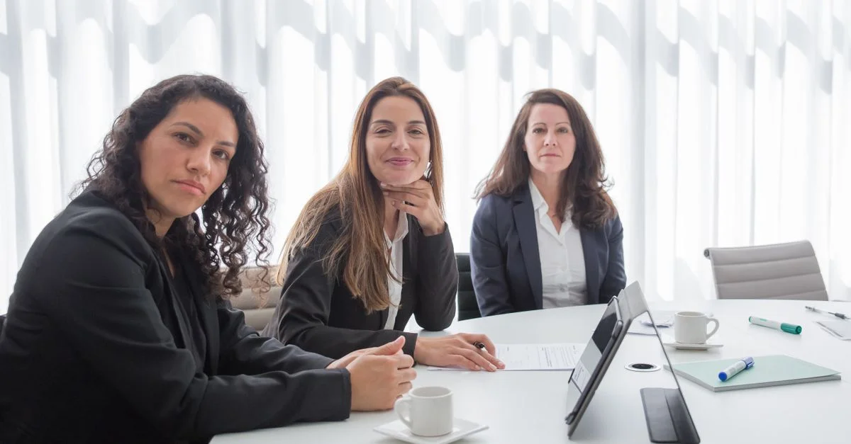 Trois femmes d'affaires dans un bureau moderne, en discussion autour d'une table de conférence.