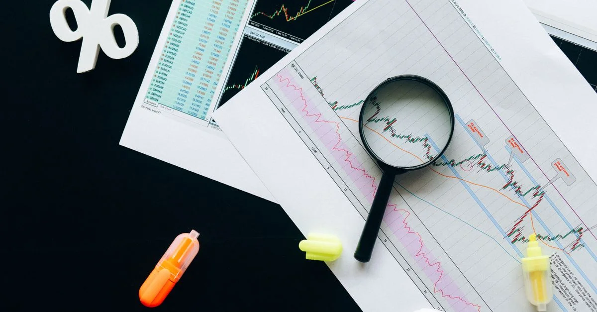 Vue en plongée sur des graphiques financiers, mettant en avant l'analyse du marché boursier avec une loupe et des surligneurs.