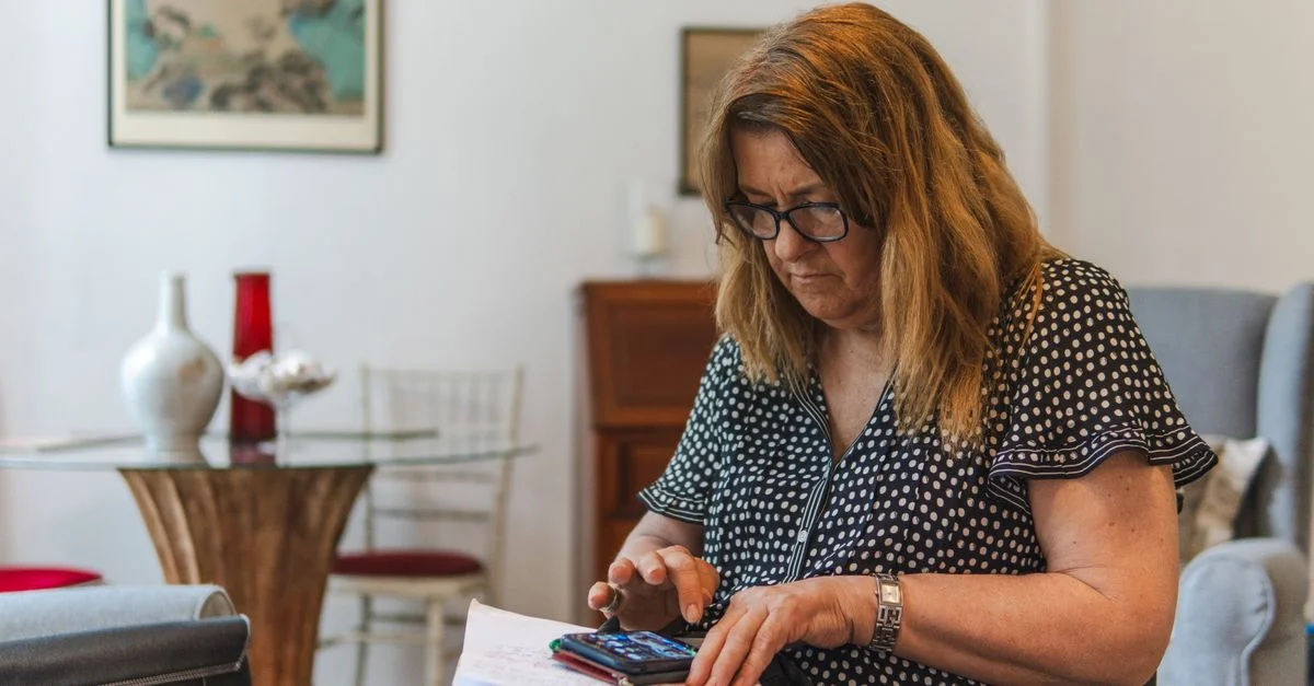 Femme concentrée calculant ses dépenses avec une calculatrice et un cahier à la maison.