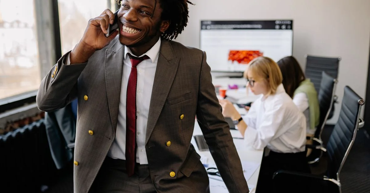 Homme d'affaires confiant avec des dreadlocks souriant tout en étant au téléphone dans un cadre de bureau moderne.