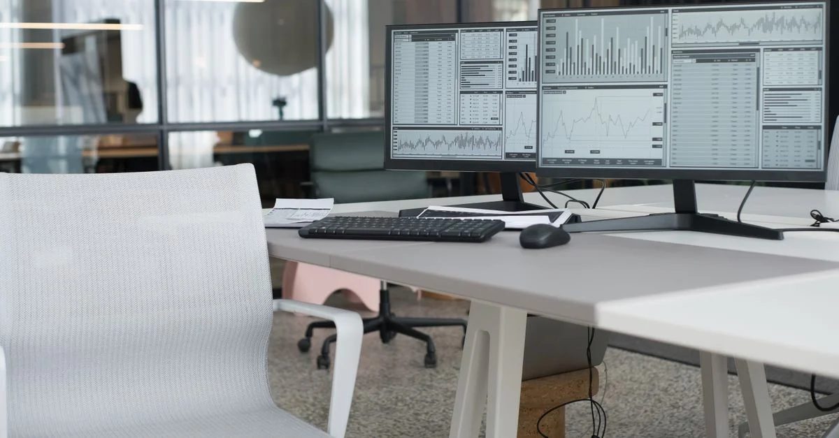 Un bureau moderne avec des moniteurs doubles affichant des données et une chaise ergonomique, parfait pour un espace de travail productif.